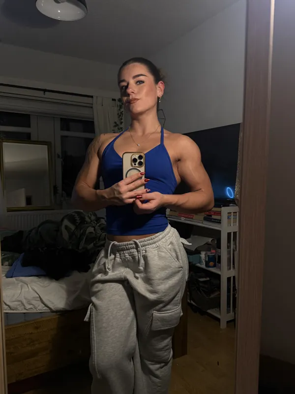 thickmouse9 mirror selfie in a blue top and grey joggers, muscular shoulders